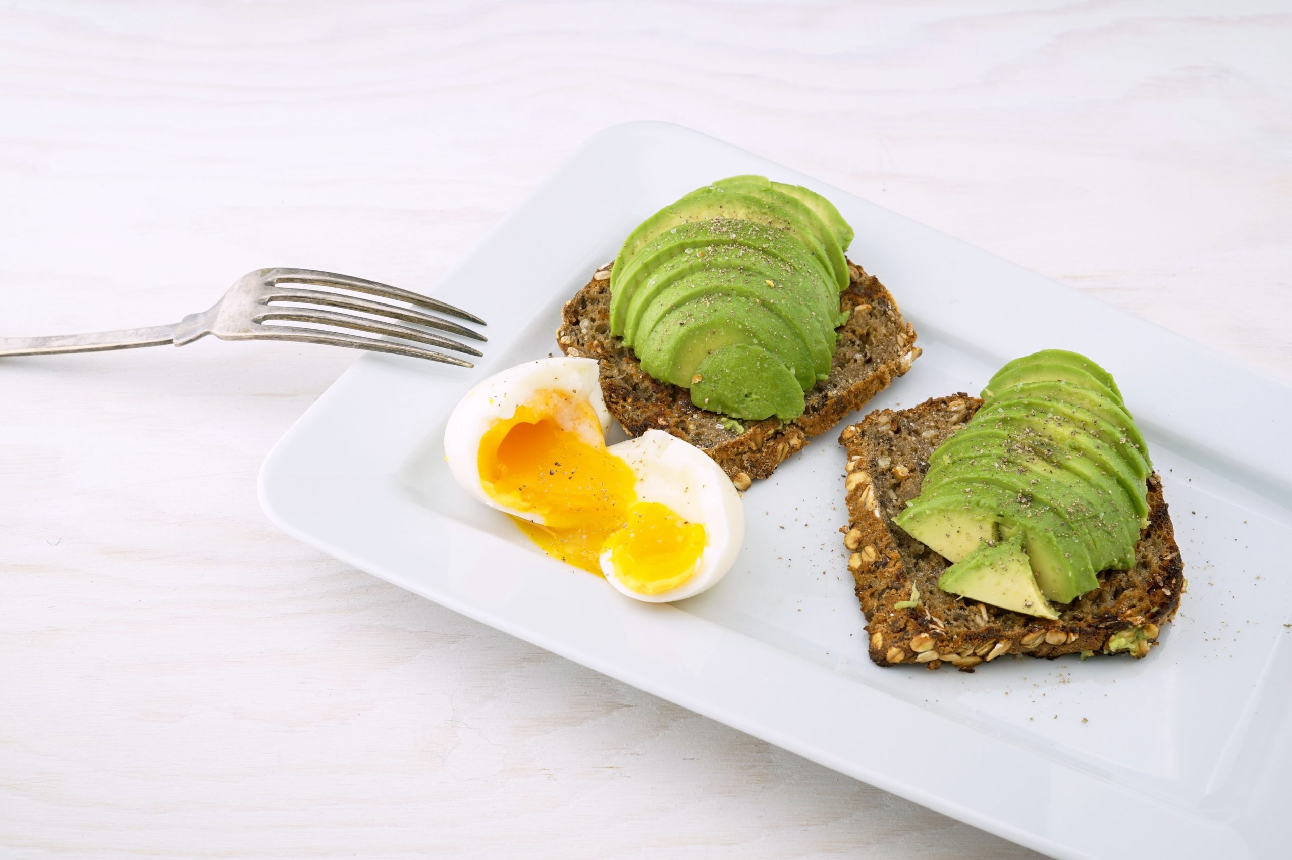 Whole wheat avocado toast on a plate with a soft-boiled egg cut in half.