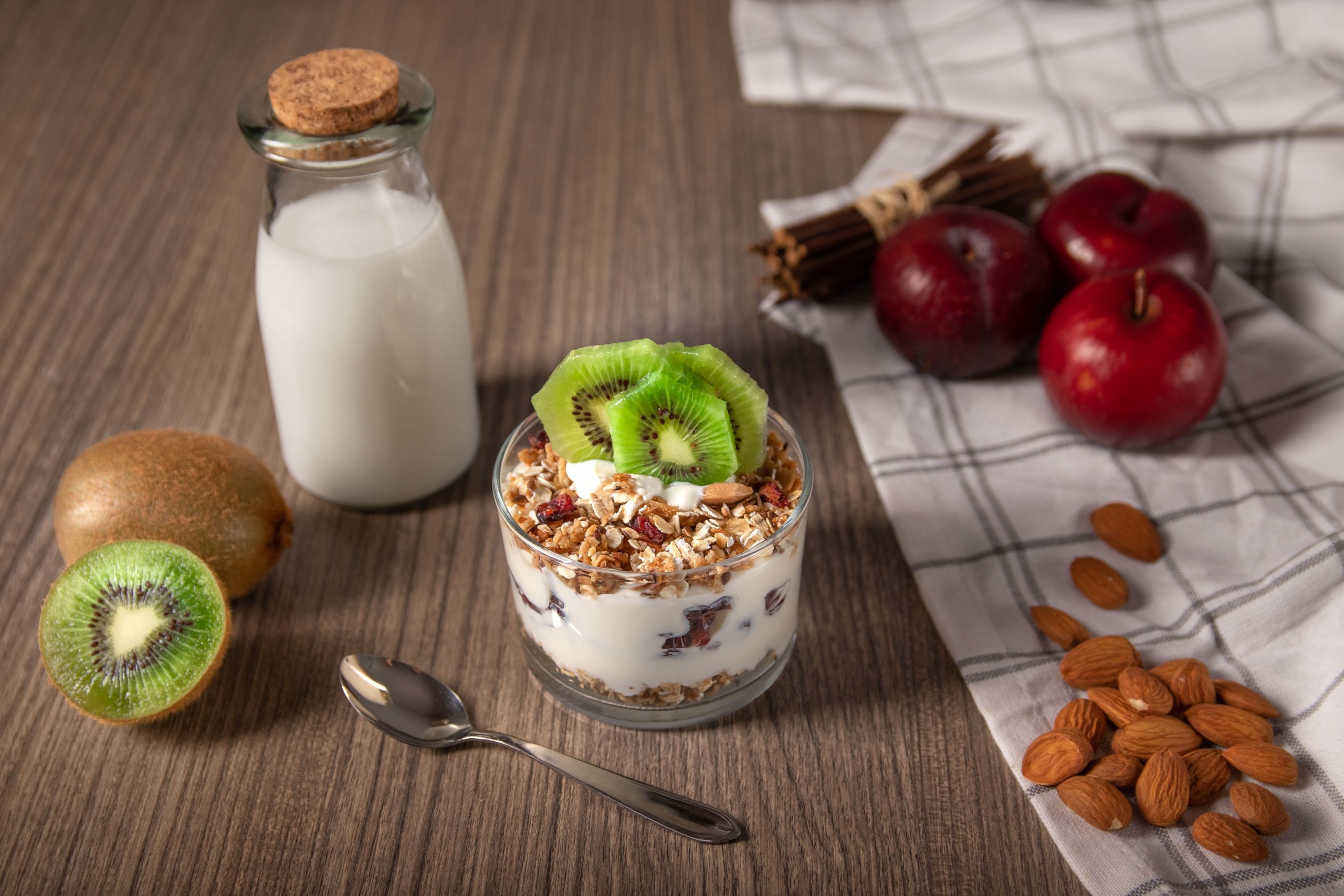 Bowl of yogurt and granola topped with kiwi. A sliced kiwi and a bottle of milk are next to the bowl. Image from Unsplash.