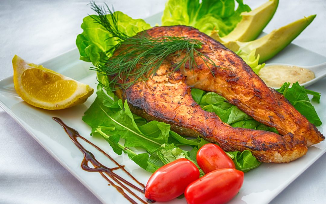 Salmon on a bed of lettuce with 3 whole tomatoes, 2 slices of avocado and a lemon wedge. Salmon is a great source of vitamin B6, as well as omega-3 fatty acids.