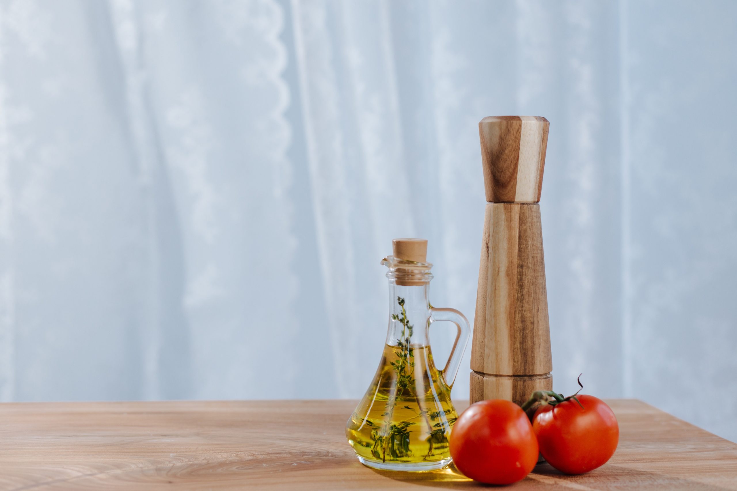 Bottle of olive oil next to a pepper shaker and two tomatoes on a vine. Olive oil is full of unsaturated fats which support brain health and function. Image from Pexels. 